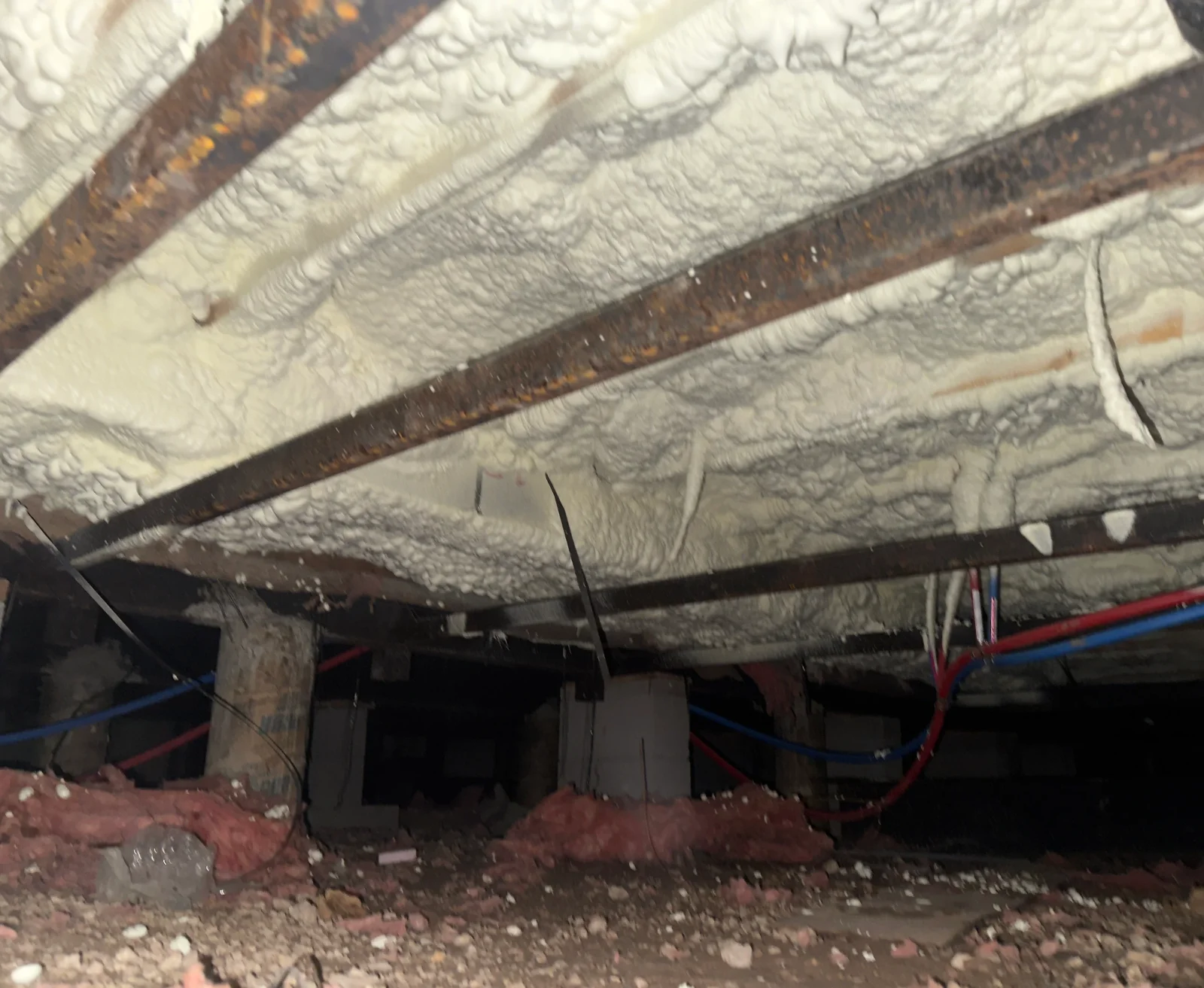 Spray foam insulation on basement ceiling with exposed steel beams and electrical wiring