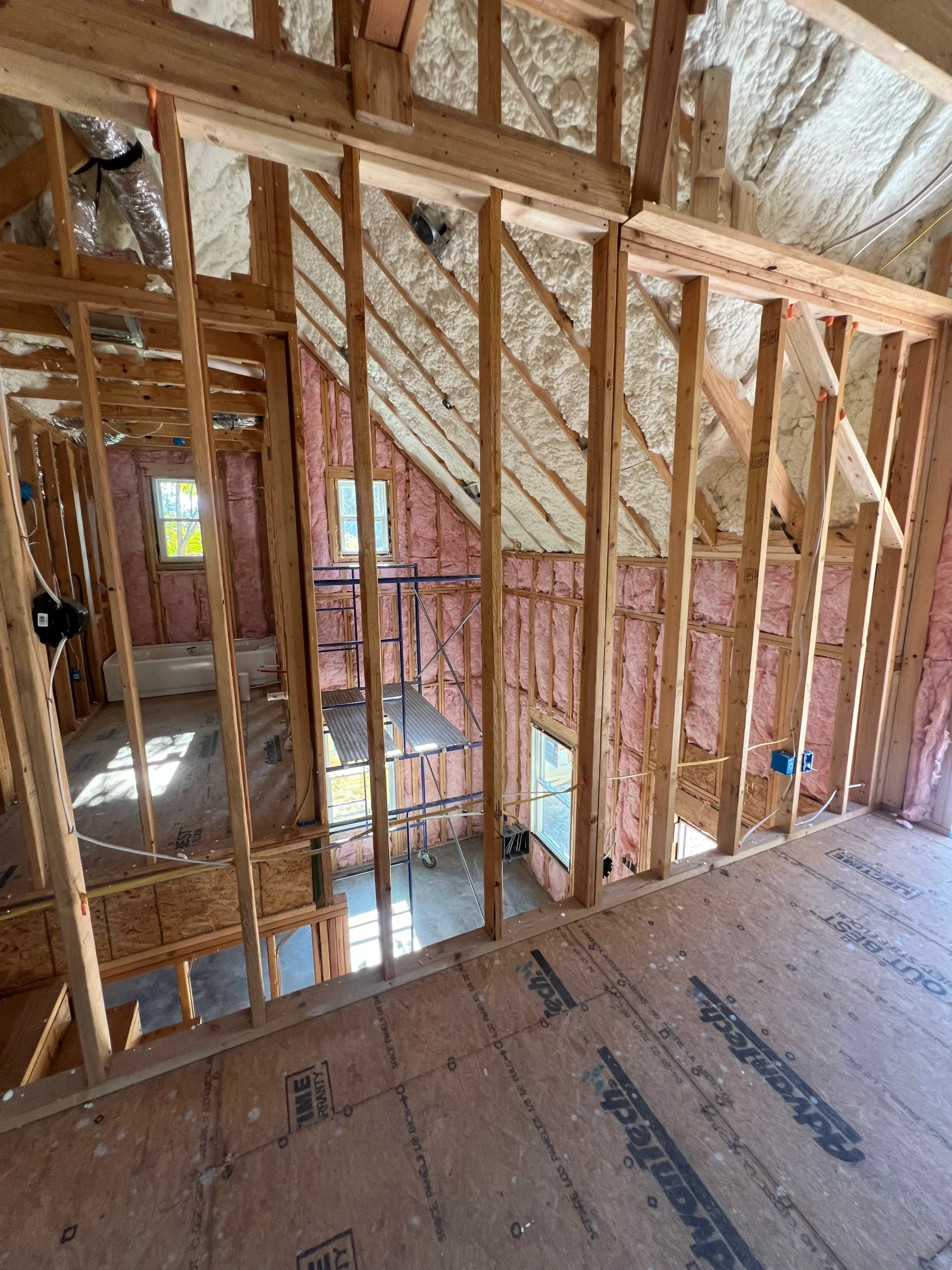 Wood framing with pink fiberglass insulation batts in walls and white blown-in insulation in attic cavity