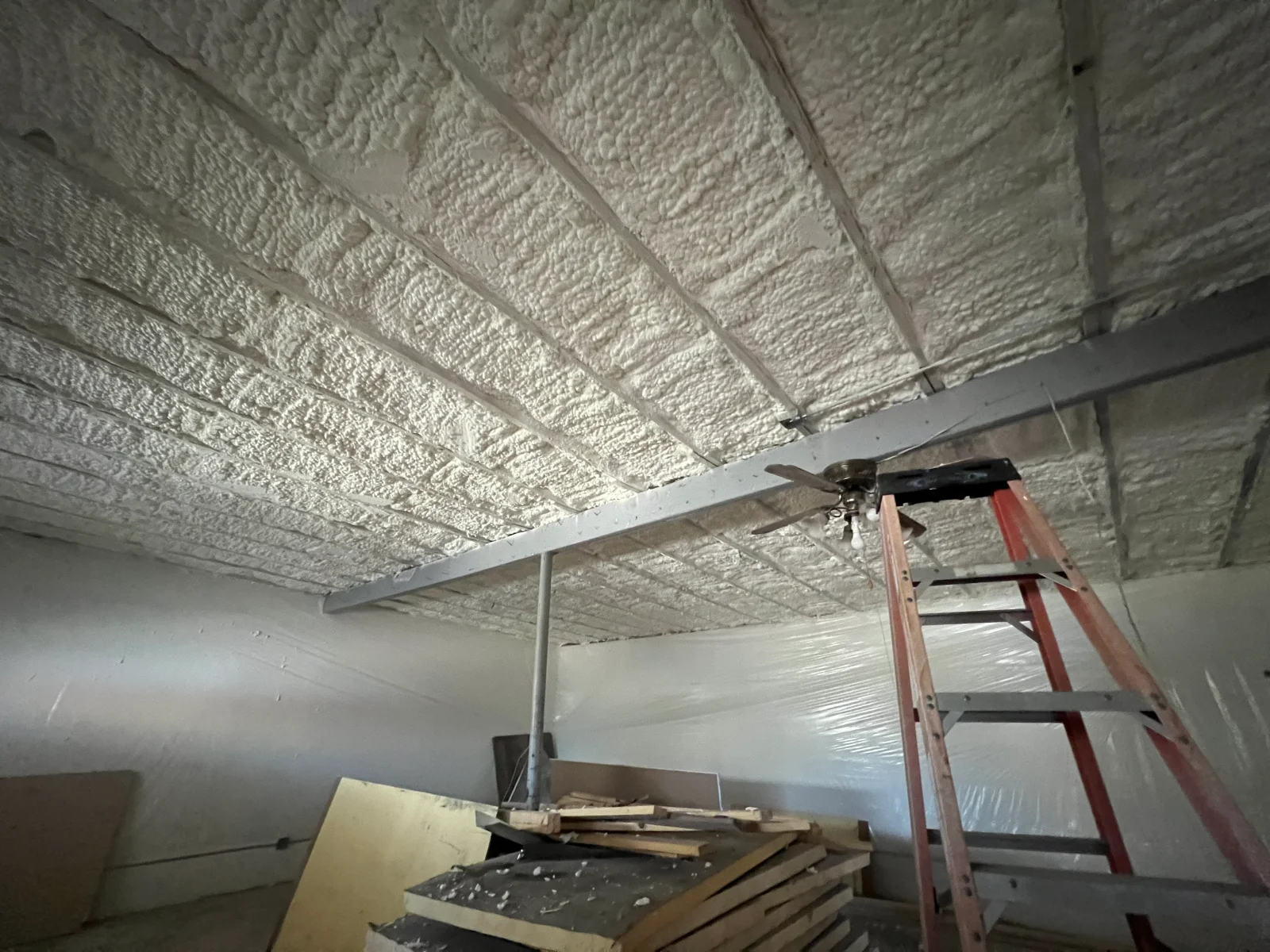 Spray foam insulation covering ceiling with metal beams and ladder for installation access