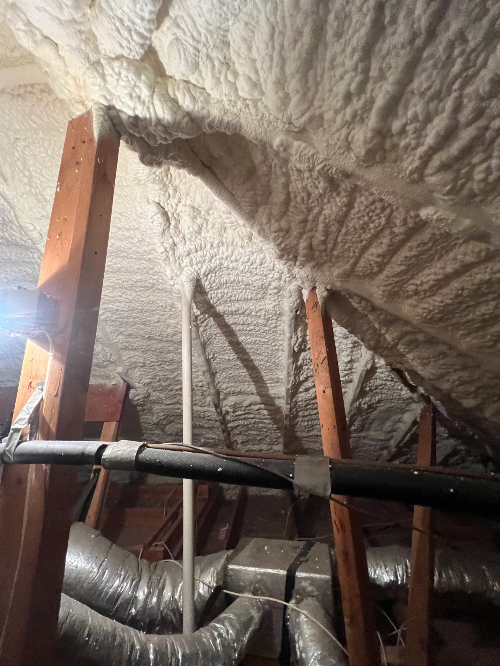 Spray foam insulation on basement ceiling with steel beam and wooden support posts
